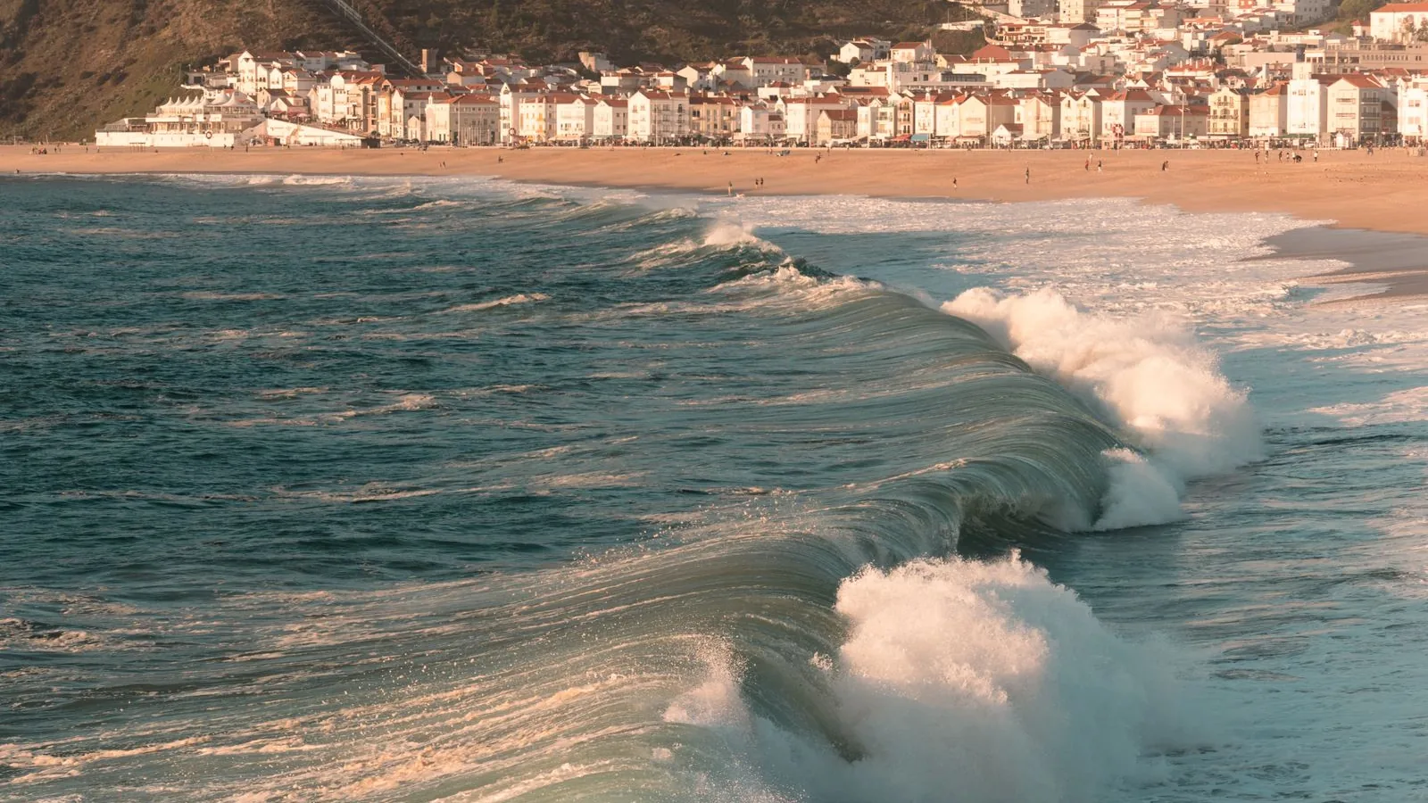 Atlantische golven breken voor de kust van Nazare, met het stadje op de achtergrond