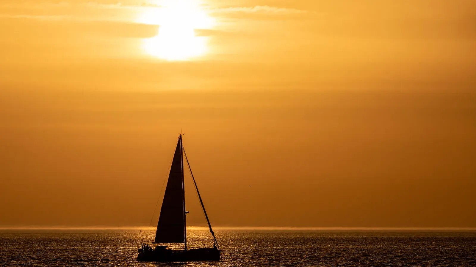 Zonsondergang boven zee met een zeilboot aan de horizon